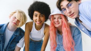 Low angle of group of cheerful multiethnic teenager friends standing together against white background and looking at camera