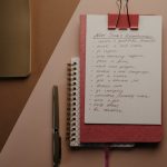 Top view of a cozy pink notebook with New Year resolutions, pen, and stylish paperclip setup.